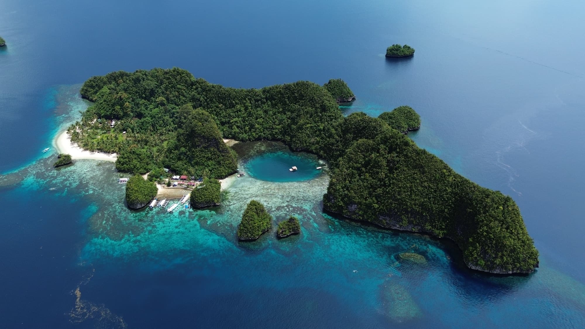 Aerial view of a circular turquoise tidal pool ringed by limestone islets and forest — the Kisses Islets and Blue Lagoon, Libjo